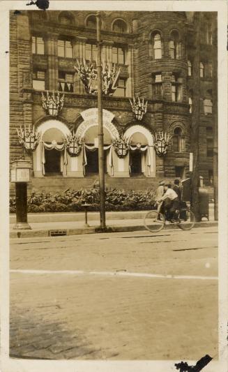 A photograph of a building decorating with bunting and flags. There is a sidewalk in front of t ...
