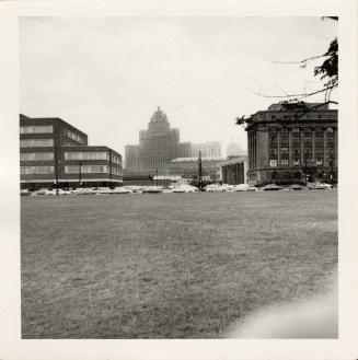 A photograph of a city skyline, with a large grassy lawn between the photographer and a group o ...
