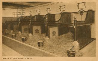 Sepia toned photograph of five very luxurious horse stalls with straw in them.