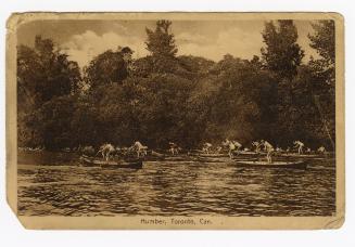 Sepia tone photograph of men and boys standing up in canoes, racing on a river.