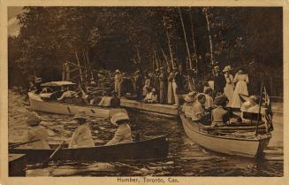 Sepia tone photograph of people sitting in boats while a crowd looks on from the shoreline.