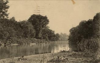 Sepia tone photograph of a person sitting in a boat on a meandering river.