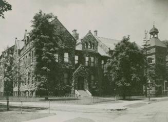 A photograph of a large three story stone building, with a sidewalk and road on the right side  ...
