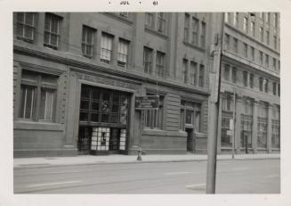 A photograph of an office building located on a city street, with a sidewalk, telephone poles a ...