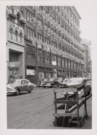 A photograph of a paved city street, with a seven story building on the left side of the photog ...