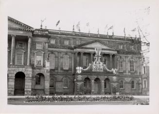 A photograph of a large stone three-story building decorated with British flags, crests and bun ...