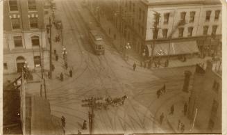 A photograph of a city intersection, taken from above. There are a horse pulling a wagon and a  ...