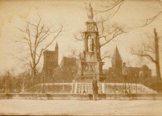 A photograph of a military monument, with a university campus building in the background. There ...
