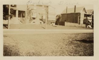 A photograph of a residential city street, with houses on the far side of the road and a grass …