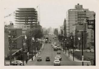 A photograph of a wide, paved city street taken from a slightly elevated vantage point. There a ...