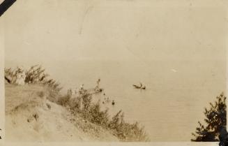 A photograph of a beach, with a dune overlooking a large body of water. There is a person sitti ...