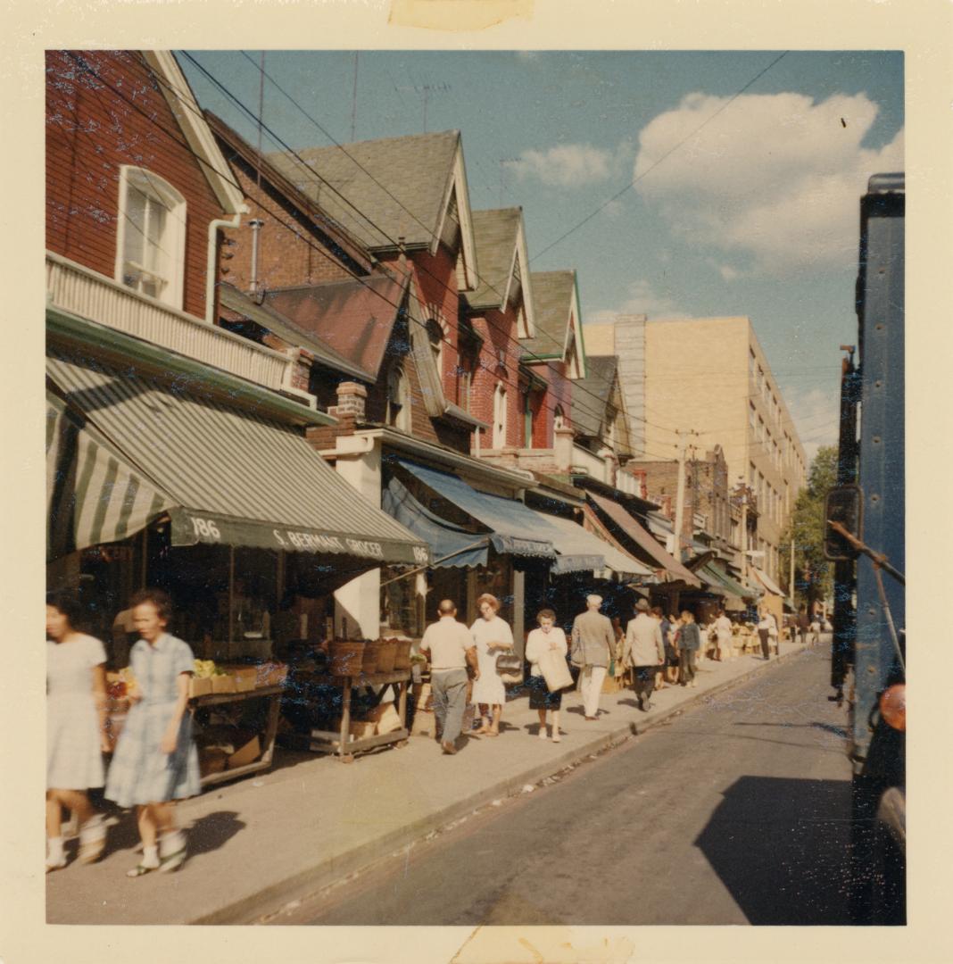 A photograph of a city street, with two and three story buildings on the left side of the road …