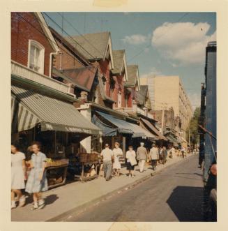 A photograph of a city street, with two and three story buildings on the left side of the road …