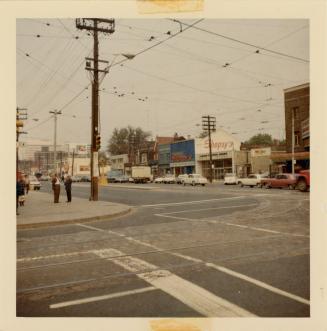 A photograph of a city street and intersection. There are crosswalks painted at two corners of  ...