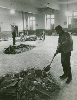 A photograph of three workers with brooms and dustpans cleaning up an interior space. There are ...
