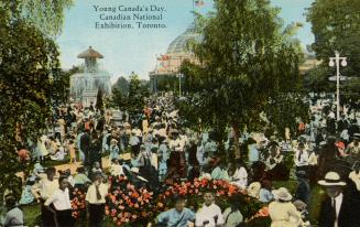Colorized photograph of a very large crowd milling around a park with a very large, marble foun ...