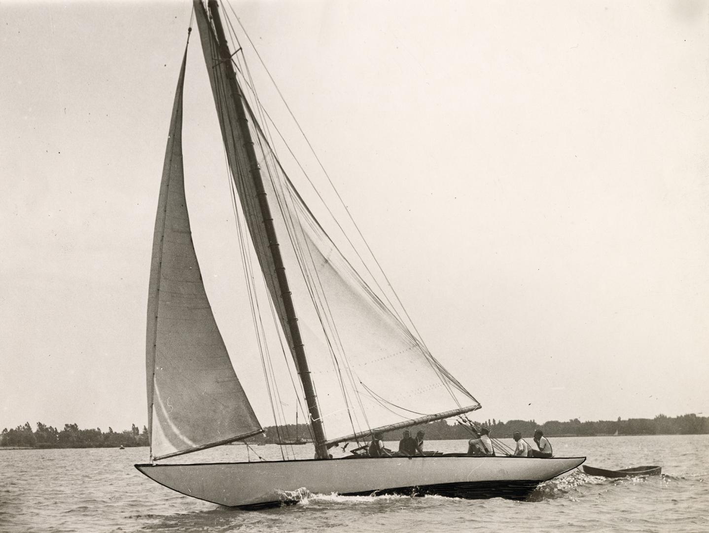 Black and white photograph of a yacht in full sail with the Toronto Islands in the background.