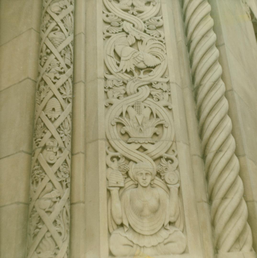 A photograph of a decorative stone engraving at the corner of a building. There are two columns ...