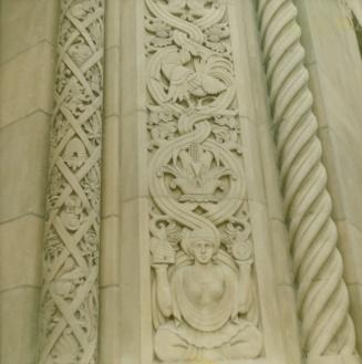 A photograph of a decorative stone engraving at the corner of a building. There are two columns…