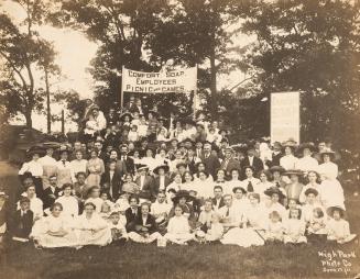 A photograph of a large group of people posing for a photograph in a park, with a grassy lawn i ...