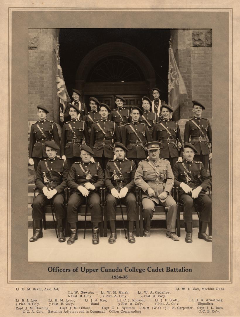 A photograph of sixteen men posing for a photograph in front of the entranceway to a large ston…