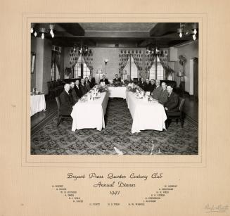 A photograph of a group of people posing around a long banquet table, which is set with dinnerw ...