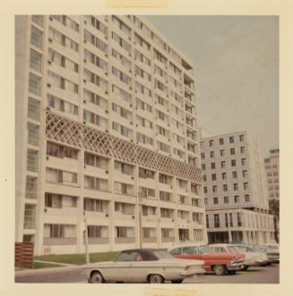 A photograph of a thirteen story apartment building, with a paved city street in front of it an ...