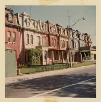A photograph of a row of three story residential townhouses with grass lawns in front, some of  ...