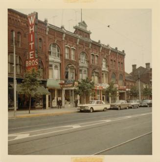 A photograph of a three story brick building, with a sign reading "WHITE BROS." on the left sid ...