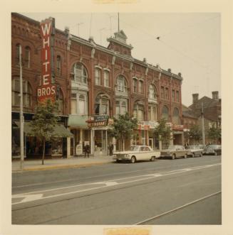 A photograph of a three story brick building, with a sign reading "WHITE BROS." on the left sid…