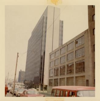 A photograph of row of warehouses and tall office buildings on the right side of a paved city s ...