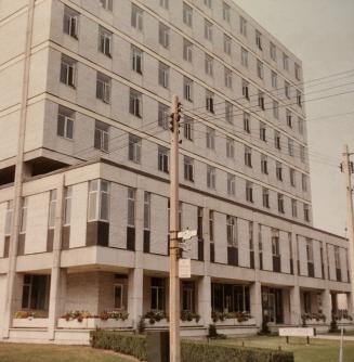 A photograph of a concrete eight story office building, with a grass lawn in front of it and ut ...
