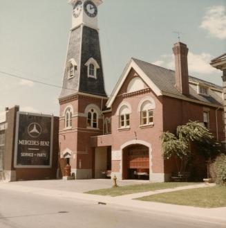 A photograph of a brick fire hall with a clock tower, and a partially open front door revealing ...