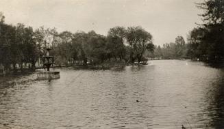 A photograph of a body of water separating wooded areas. There is a five-tiered fountain on the ...