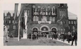 A photograph of a large stone building decorated with bunting, banners and flags. There is a pa ...