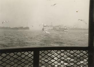 A photograph taken from the passenger area of a ferry, with a large body of water and other boa ...
