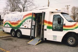 Picture of a parked bookmobile van with accessible ramp and rainbow design. 