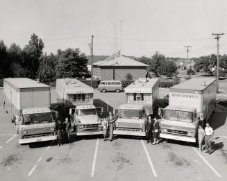 Picture of four bookmobiles parked in a semi circle and two staff members standing by each. 