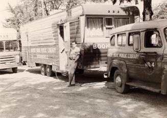Picture of man leaning against bookmobile trailer with van hooked up to it. 