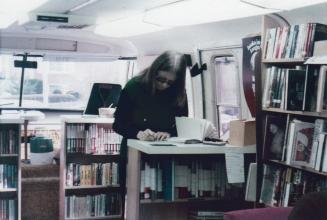 Interior of bookmobile with staff member standing writing at desk. 