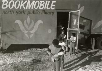 Several children holding books come out of the door of a bookmobile. 
