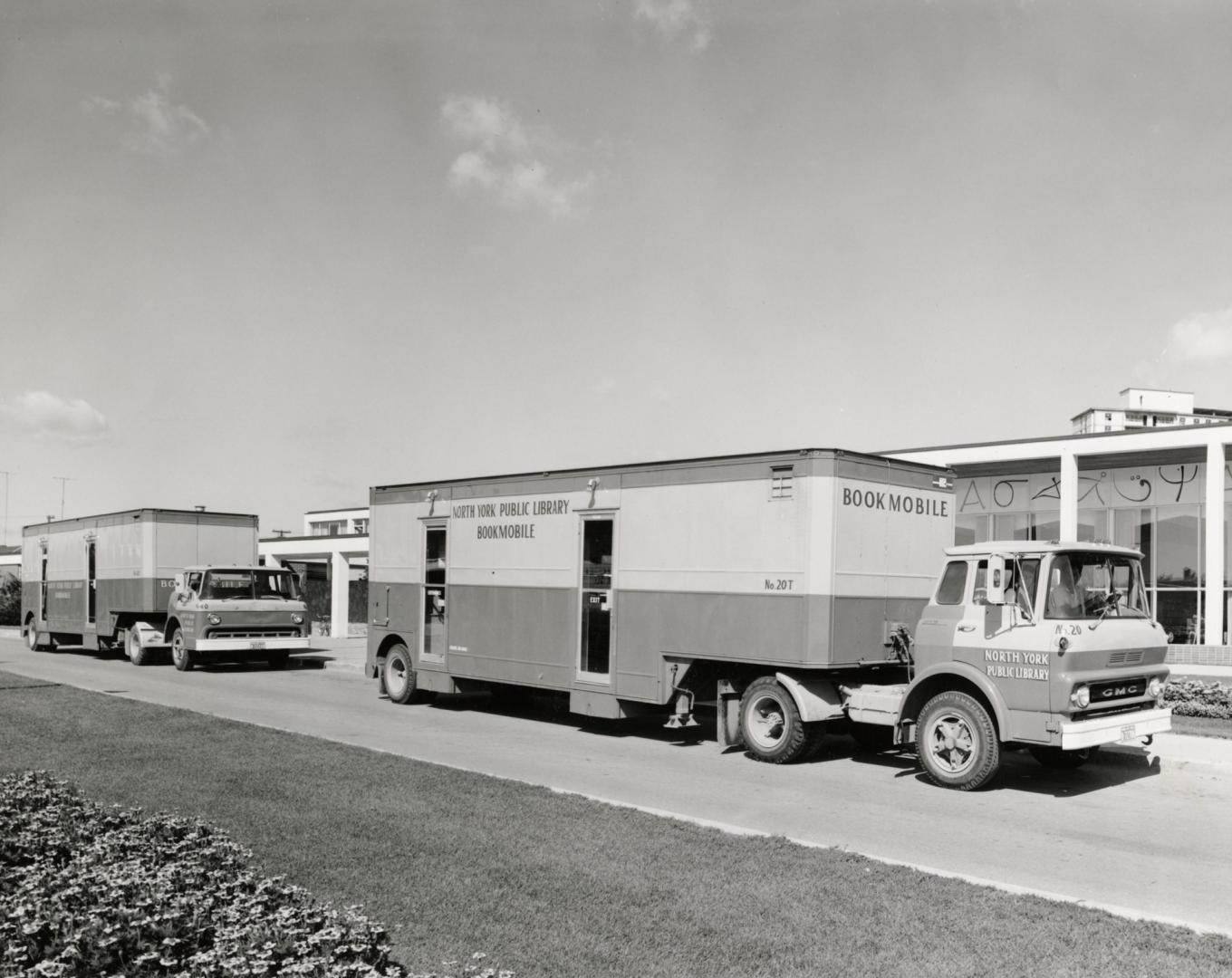 Two bookmobiles parked outside a library building. 