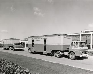 Two bookmobiles parked outside a library building. 