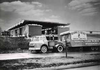 Picture of a bookmobile parked in front of library building under construction. 