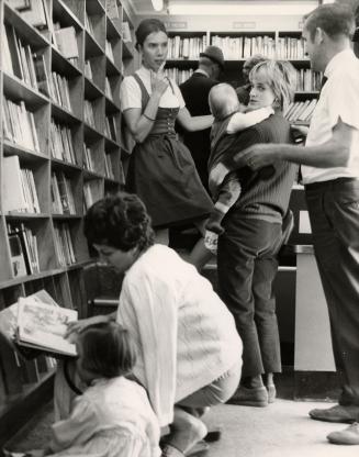 A group of people inside a bookmobile with a woman and child crouching looking at books and oth ...