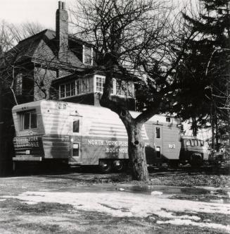 Picture of a bookmobile parked beside a house and large tree.