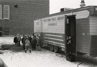 Group of children waiting at the entrance to a bookmobile, 1 child exiting the bookmobile