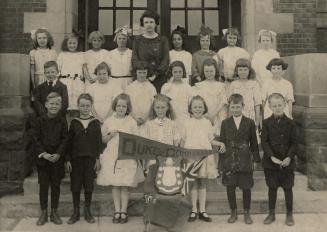 Picture of a school choir with children standing on the school steps holding banner and trophy. ...