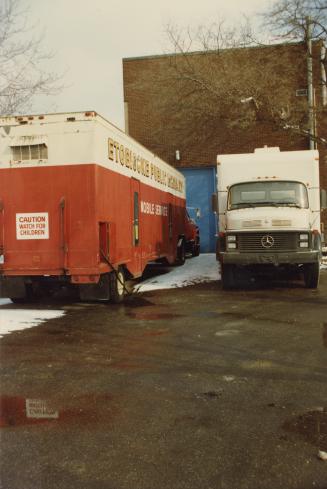 Picture of red and white bookmobile parked next to white truck bookmobile. 