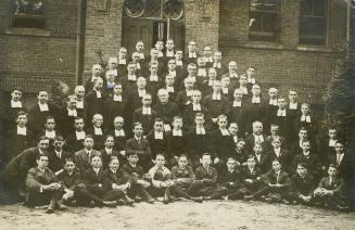 Black/white photo postcard depicting the Brothers, novices, and junior novices (students) of De…